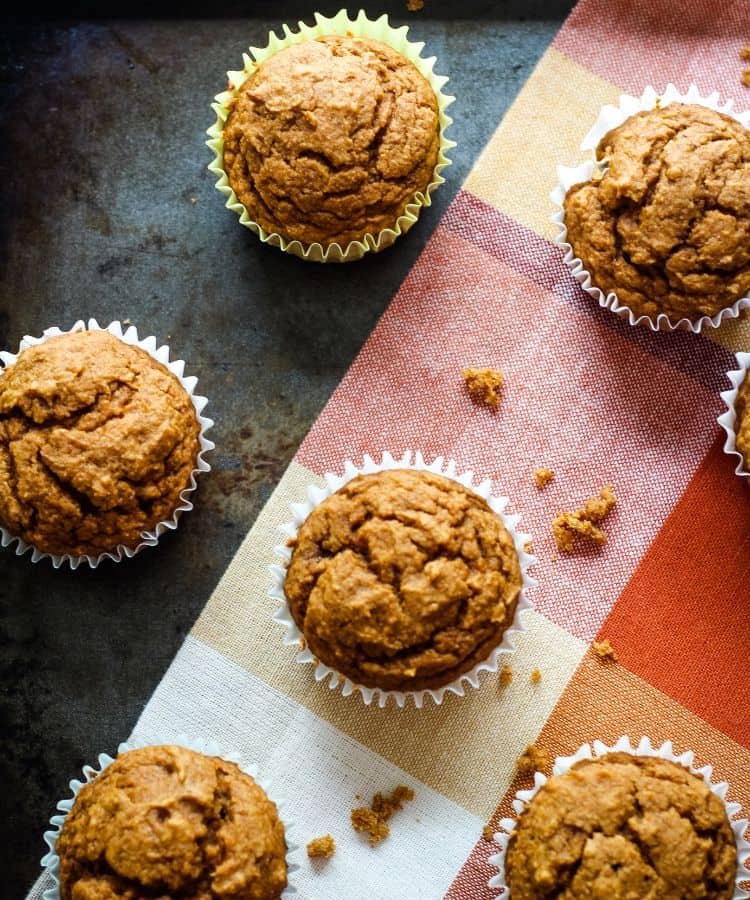 Vegan pumpkin muffins on baking sheet lined with orange plaid napkin.