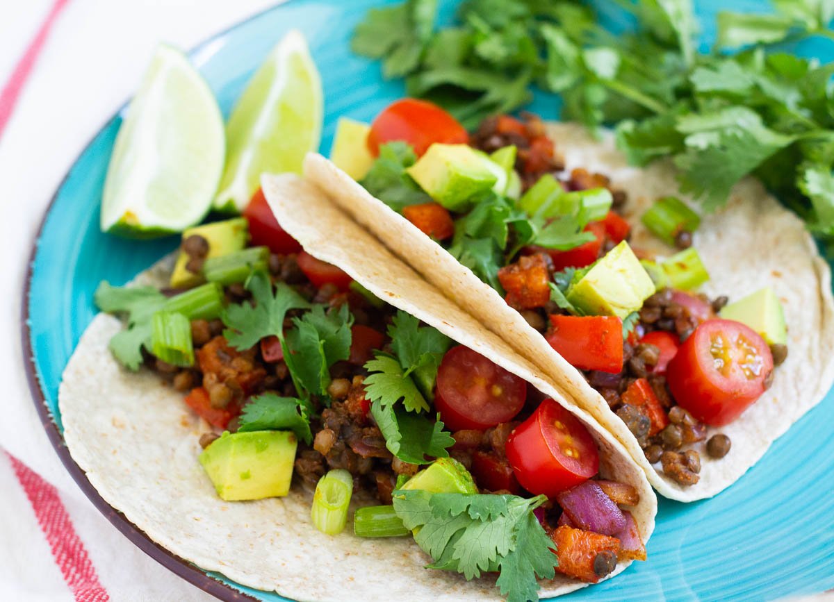 Vegan tacos filled with lentils diced avocado, diced tomato, and scallions.