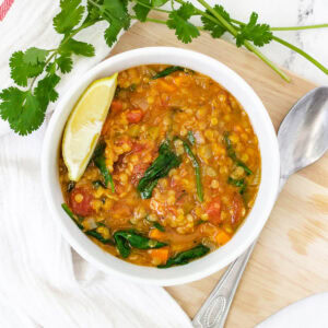 Low calorie lentil soup with spinach and lemon wedge in white bowl.