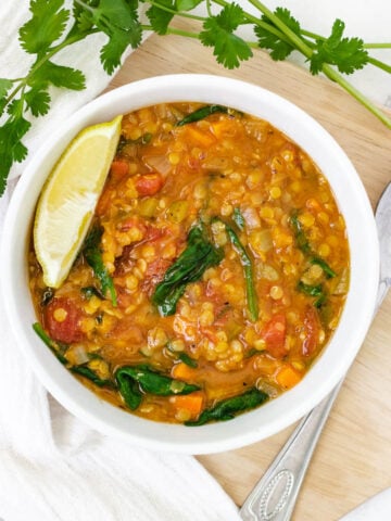 Low calorie lentil soup with spinach and lemon wedge in white bowl.