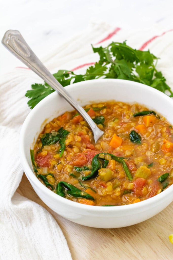 Bowl of healthy lentil soup with spinach and tomatoes with spoon inside.