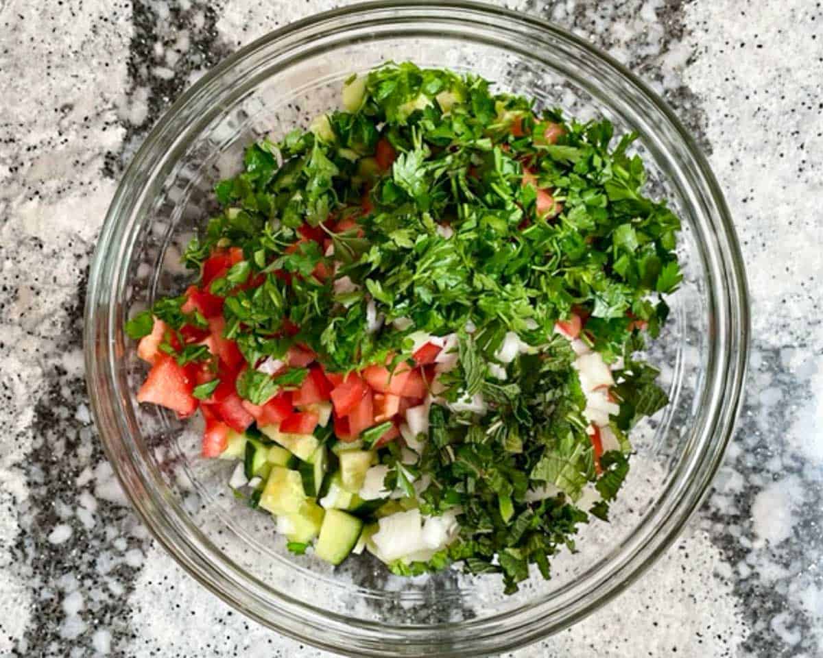 Parsley, mint, cucumbers, and tomatoes in large glass bowl.