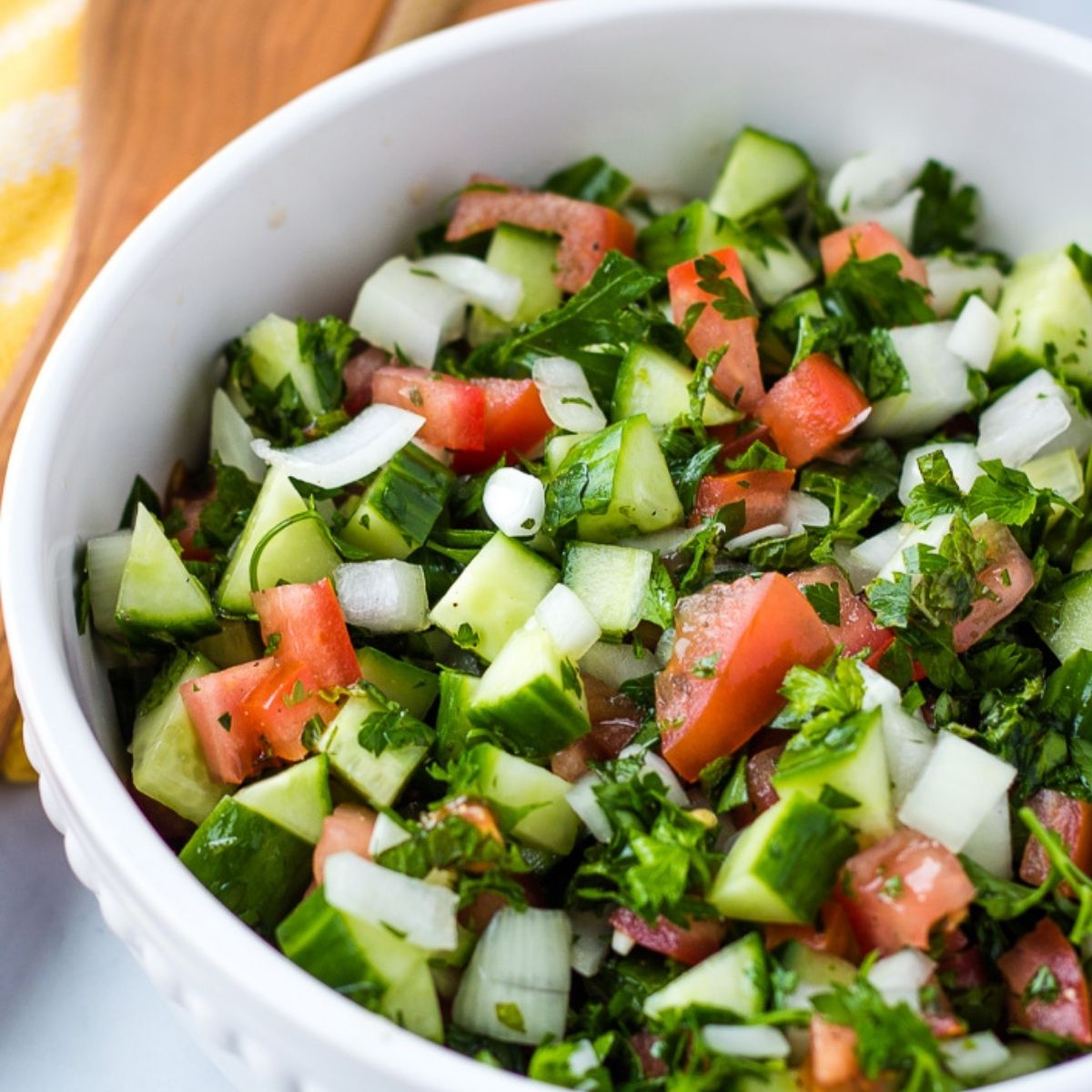 Mediterranean cucumber salad with fresh herbs, tomato and onion in a white serving bowl. 