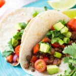 Whole wheat tacos filled with vegan taco meat, and topped with diced avocado, tomato, scallions, and cilantro.