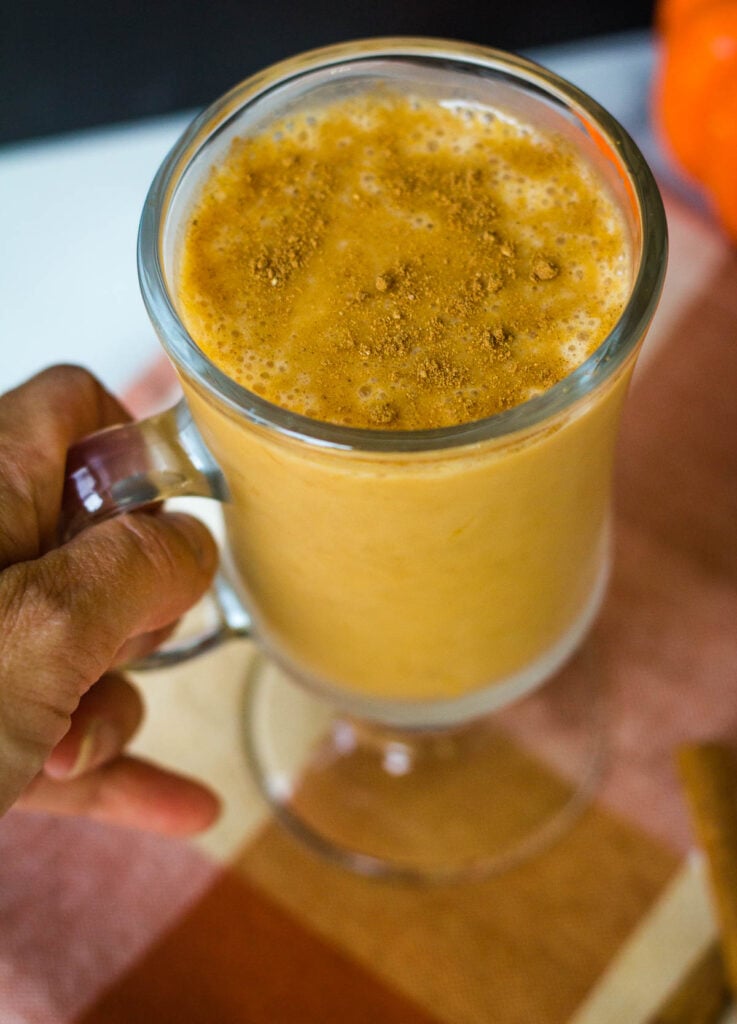Hand holding mug filled with pumpkin smoothie and topped with pumpkin pie spice.