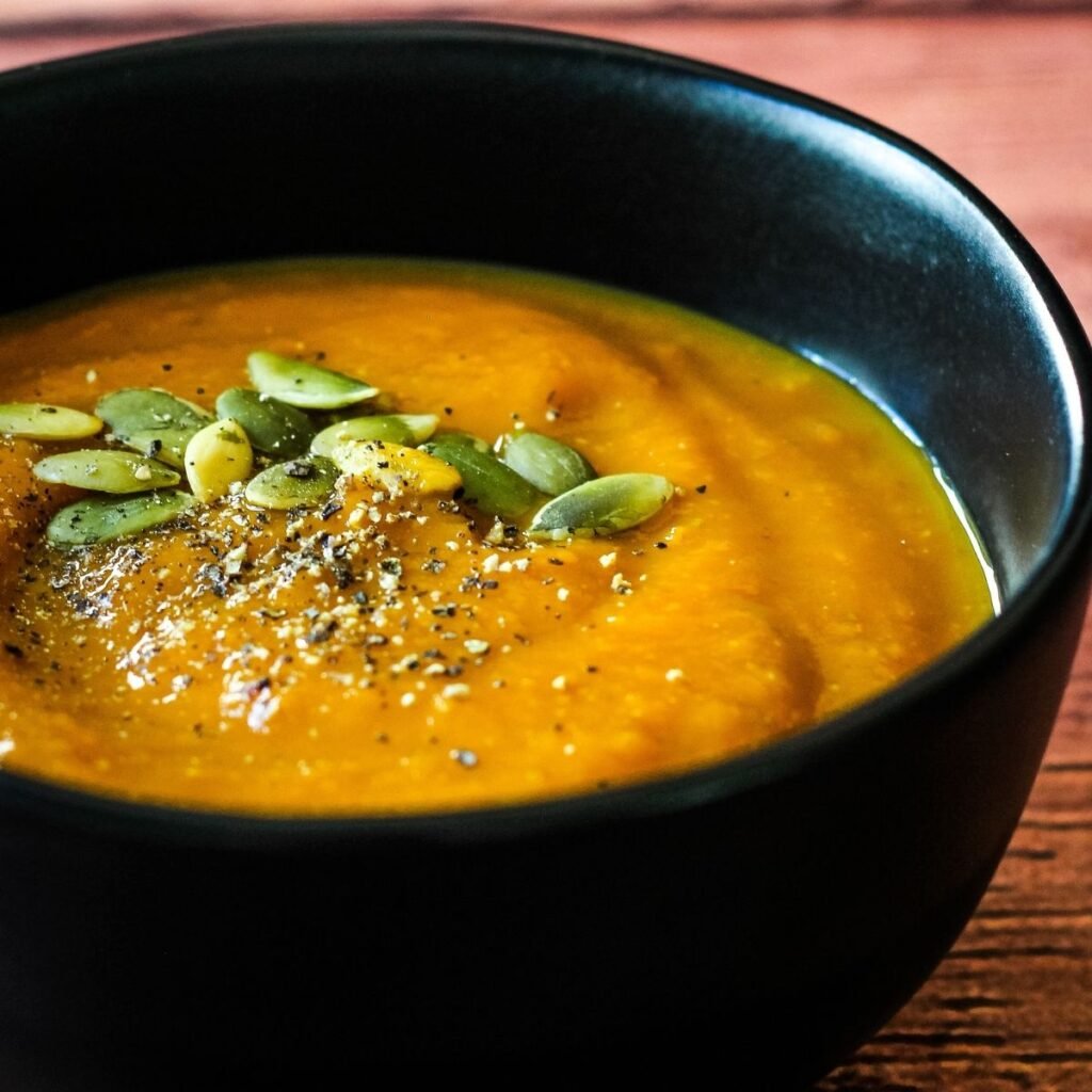 Vegan pumpkin soup topped with pumpkin seeds and black pepper in black bowl.