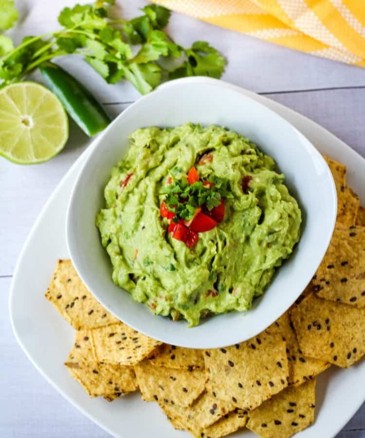 traditional guacamole in white bowl surrounded by chips