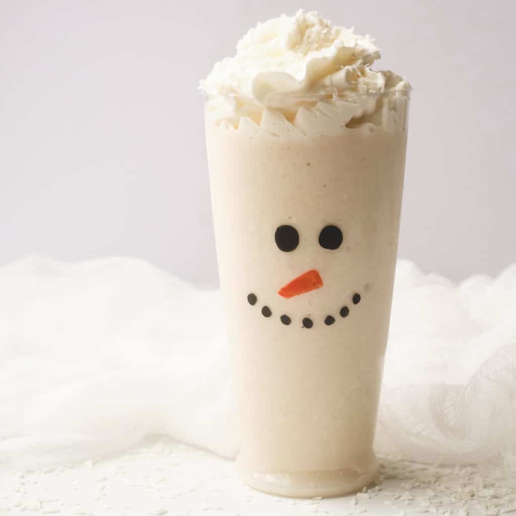 Snowman Christmas smoothie topped with whipped cream in tall glass.