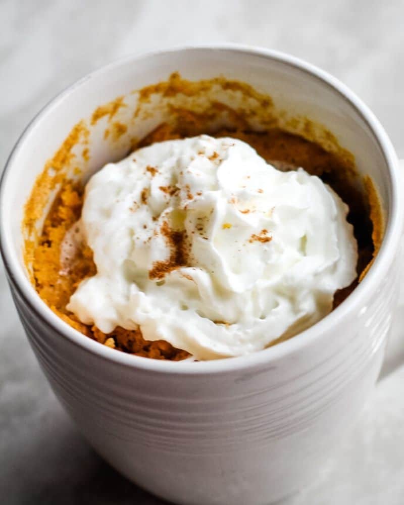 Pumpkin mug cake topped with whipped cream and pumpkin pie spice.