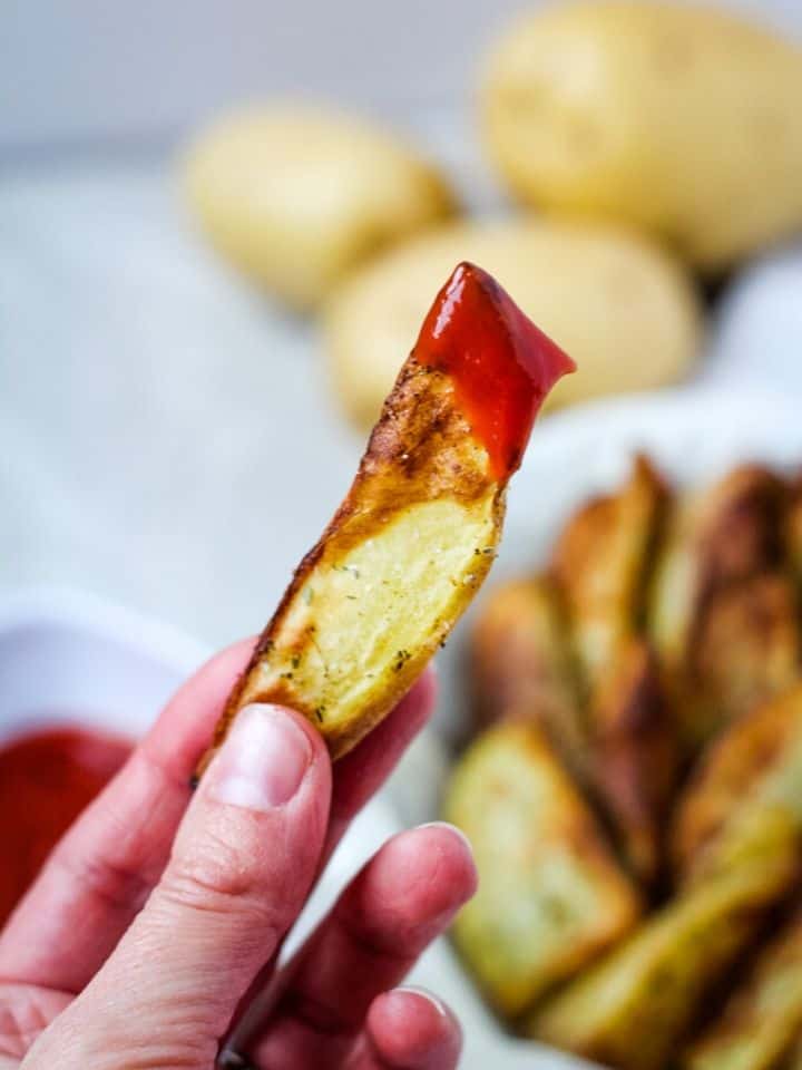 hand holding homemade fry dipped in ketchup