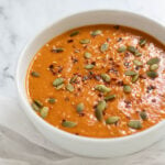 Bowl of butternut squash and red pepper soup topped with red pepper flakes and pumpkin seeds.