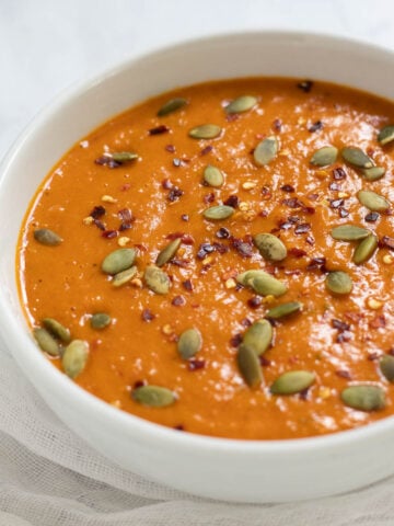 Bowl of butternut squash and red pepper soup topped with red pepper flakes and pumpkin seeds.