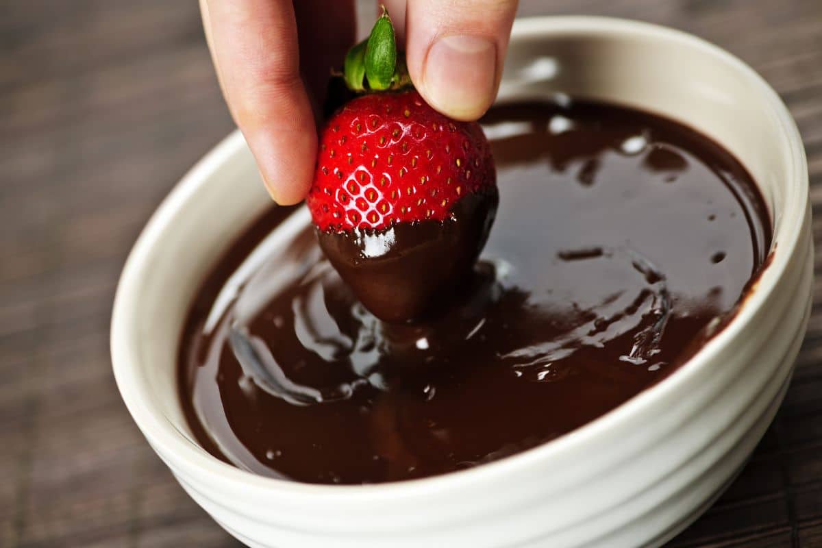 Dipping a strawberry into melted chocolate.