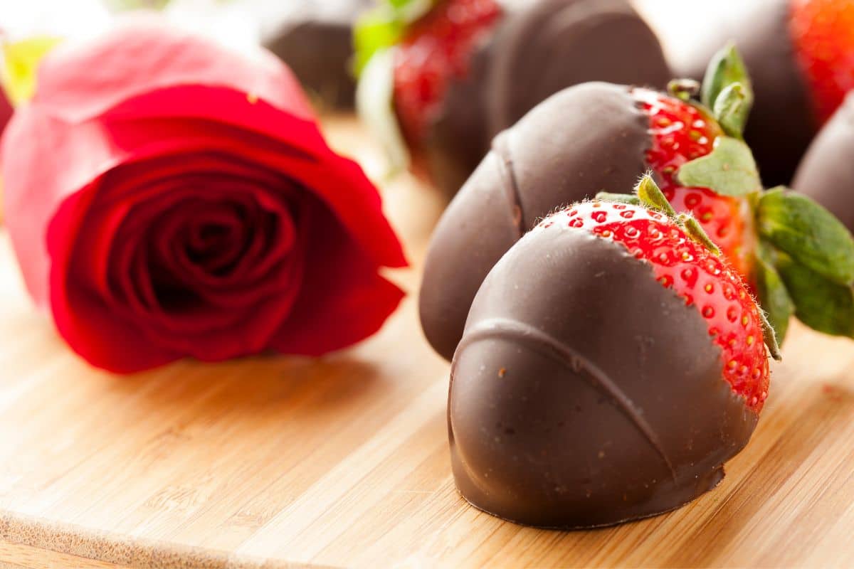 Vegan chocolate covered strawberries beside a red rose.