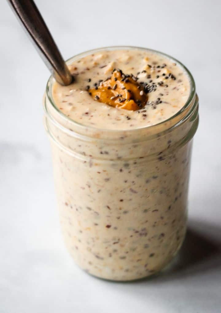 close up peanut butter overnight oats in mason jar with spoon topped with peanut butter, and chia seeds