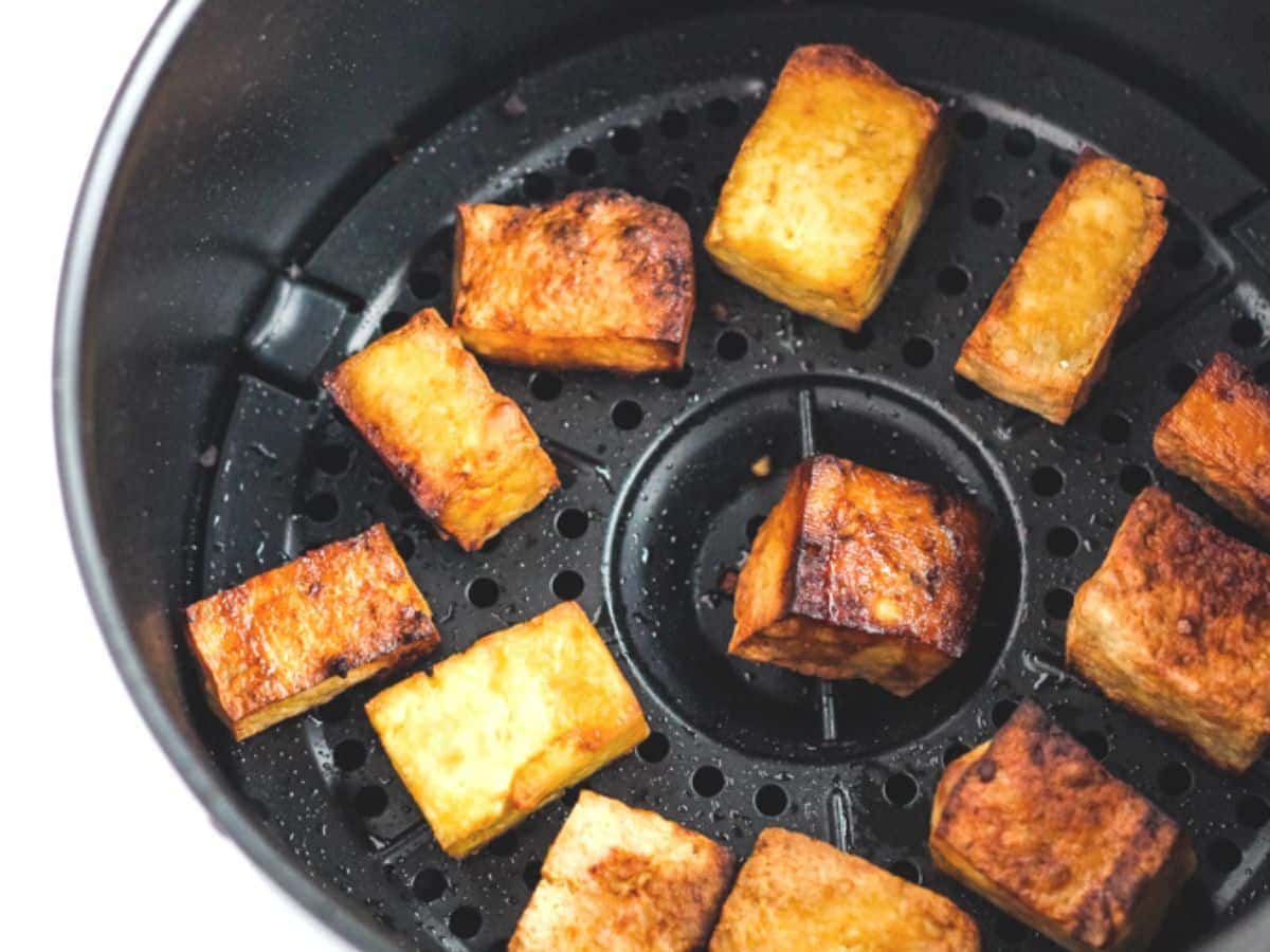 Crispy spicy air fryer tofu cubes in air fryer basket.