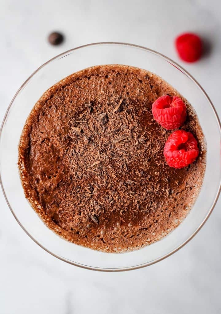 close up overhead shot of aquafaba chocolate mousse topped with chocolate shavings and two raspberries