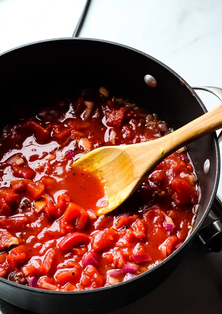 Stirring diced tomatoes with a wooden spoon in a large pot.
