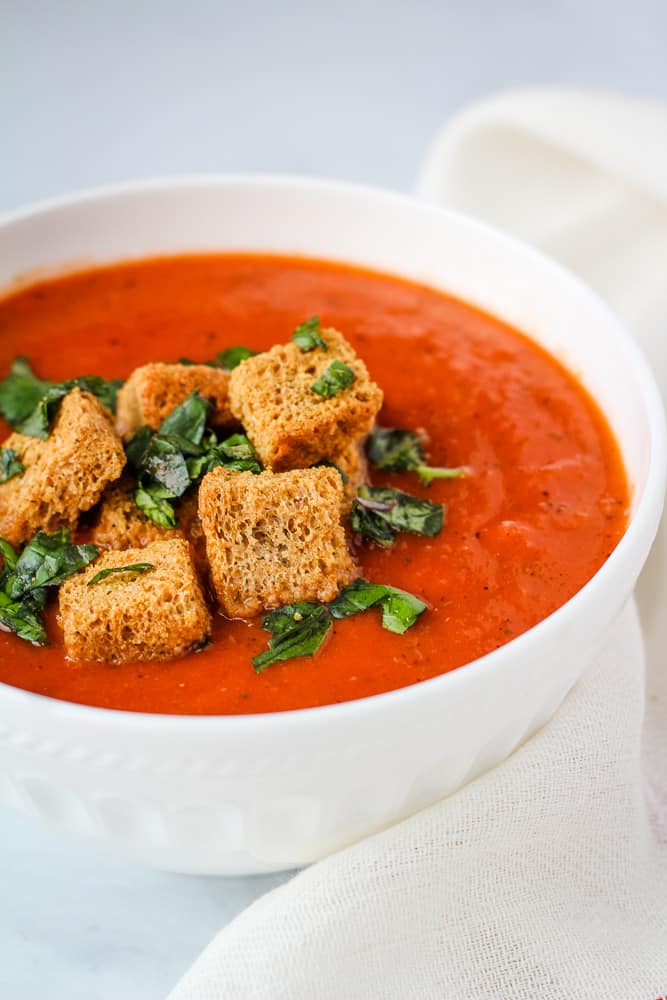 Bowl of creamy vegan tomato soup topped with croutons and fresh basil.
