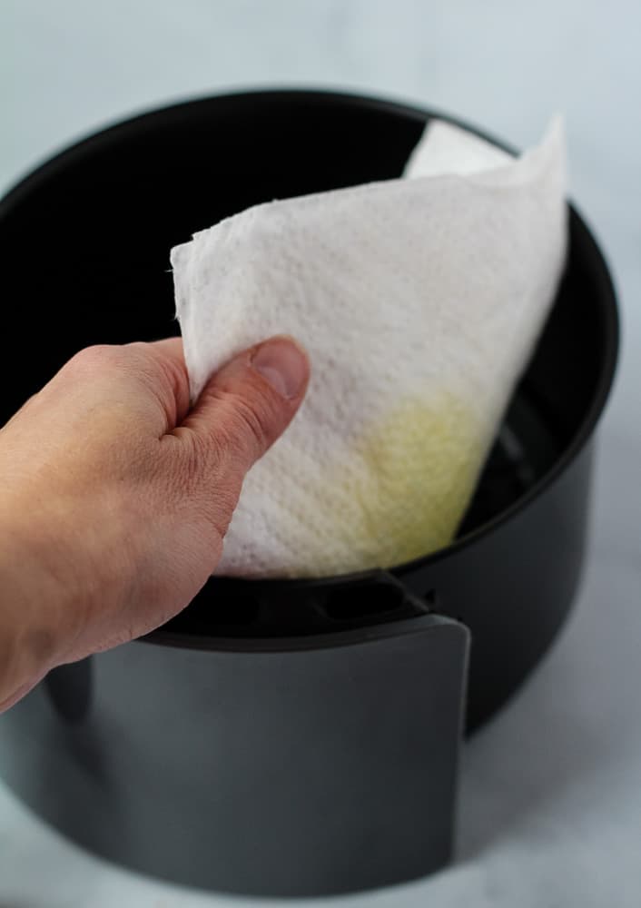 hand wiping air fryer basket with paper towel