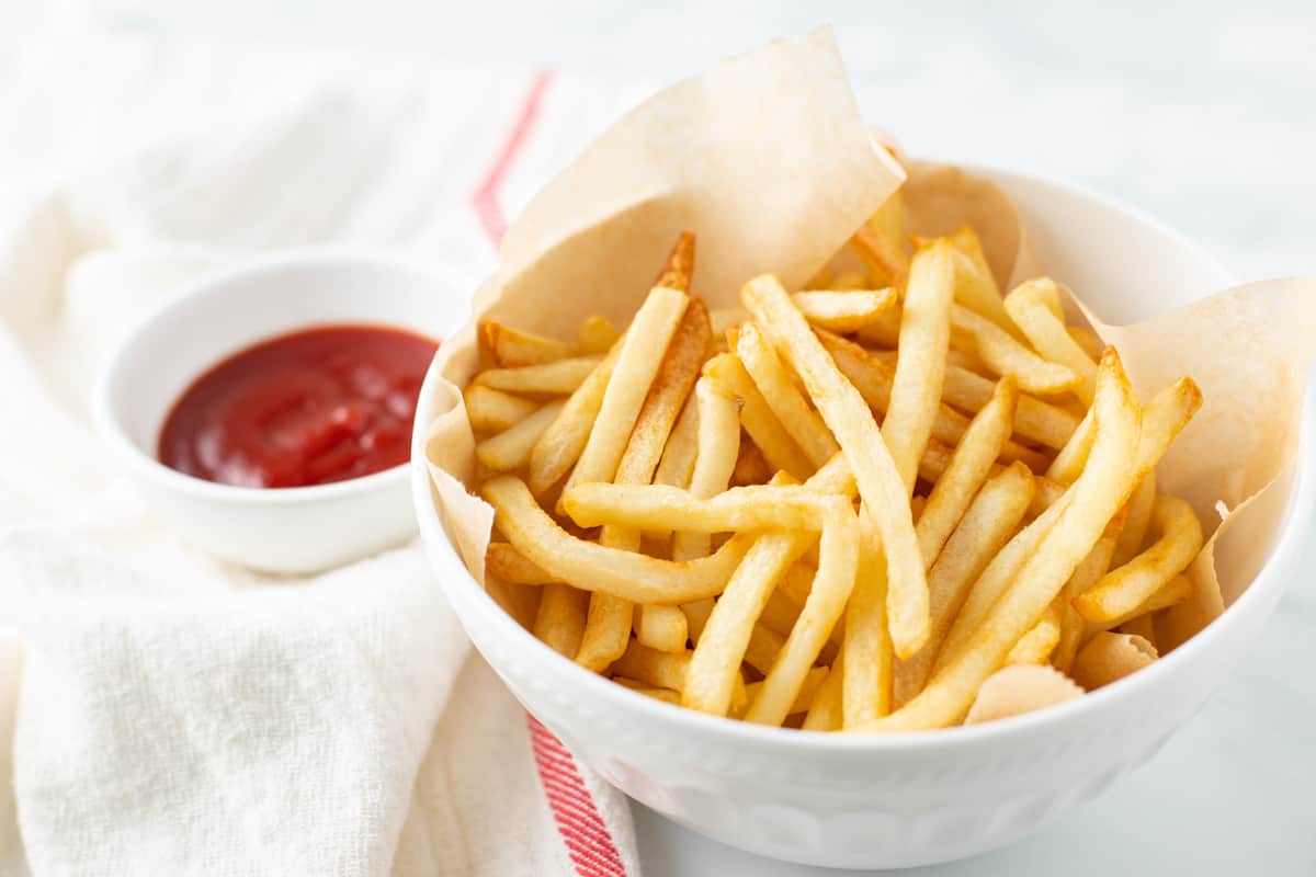 Shoestring fries in white bowl served with a side of ketchup.
