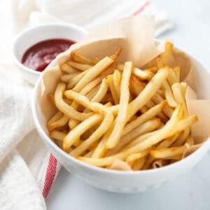 Air fryer shoestring fries in white bowl with a side of ketchup.