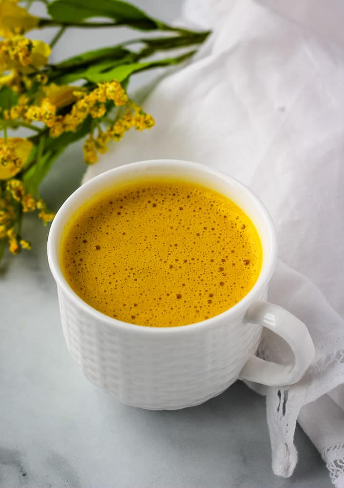 Mug of golden milk latte beside dried yellow flowers.