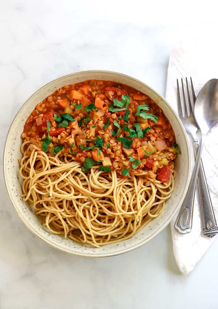 Vegan lentil bolognese served with whole wheat spaghetti in wide bowl.
