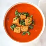 Bowl of tomato soup with croutons and fresh herbs.