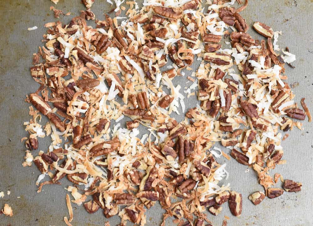 Chopped pecans and coconuts spread on baking sheet.