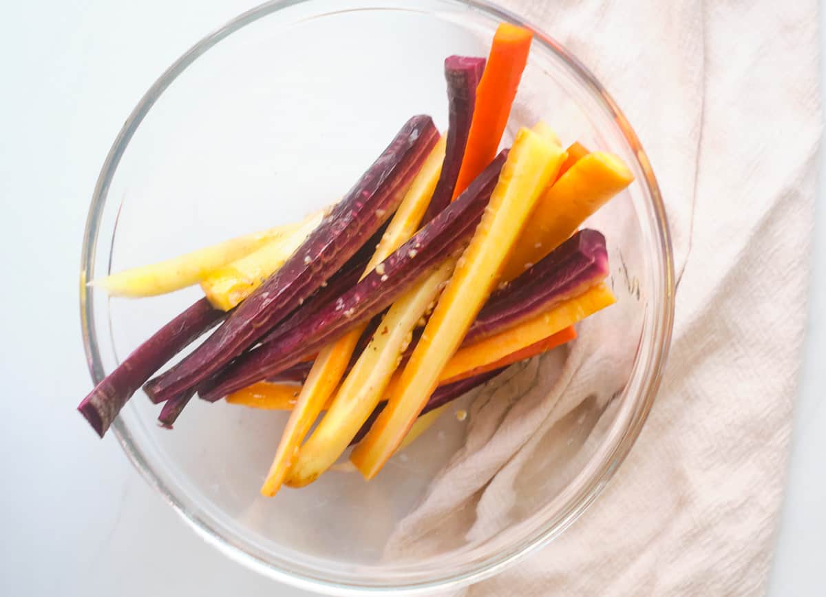 Rainbow carrots in glass bowl topped with seasoning. 