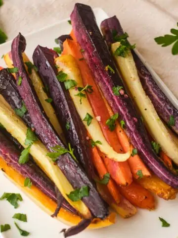 Air fryer rainbow carrots on white square plate topped with fresh herbs.