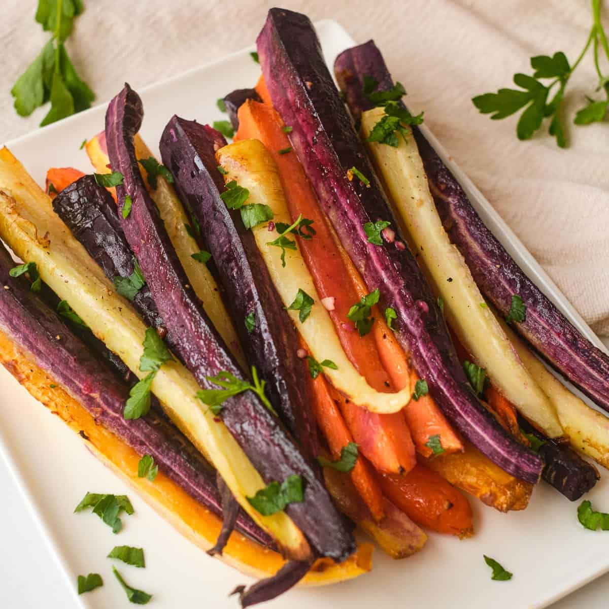 Air fryer rainbow carrots on white square plate topped with fresh herbs.