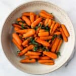 Roasted baby carrots in shallow bowl topped with chopped greens.