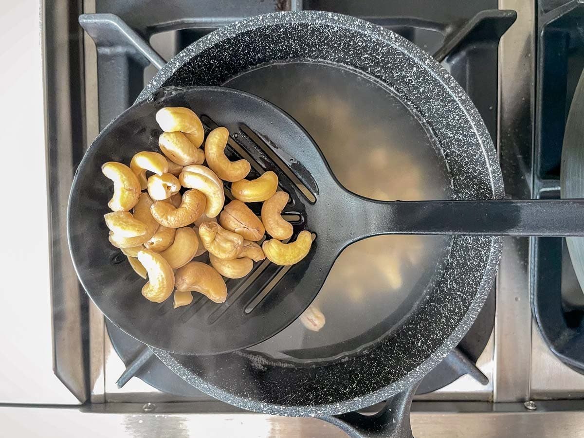 Boiled cashews on slotted spoon over pot of water.