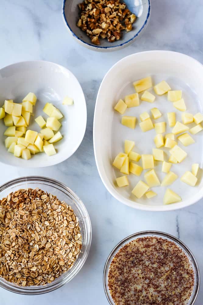 Apples, oats, walnuts and flax almond milk on bowls.