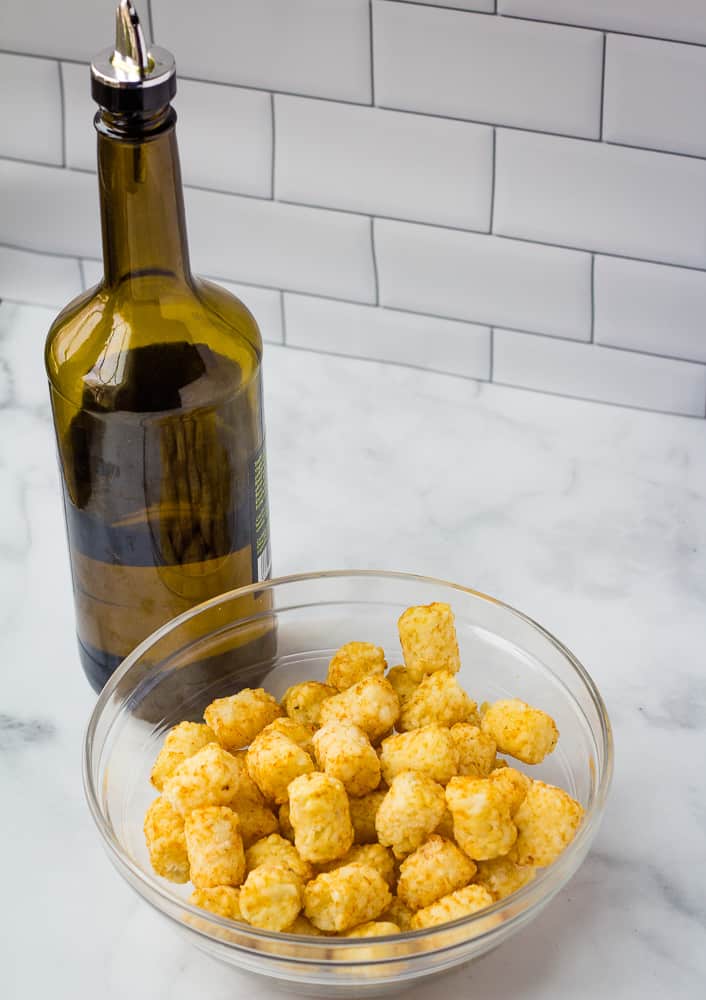 Bowl of frozen tater tots, and jug of olive oil on counter top.