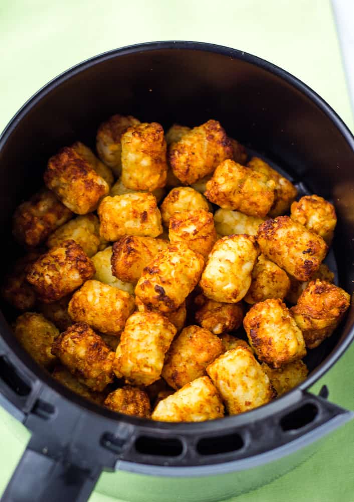 Crispy golden brown frozen tater tots in air fryer basket after they've been cooked.