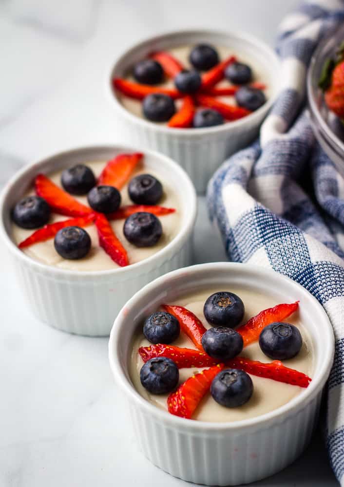 Vanilla pudding in white ramekins, topped with strawberry and blueberries in star pattern.