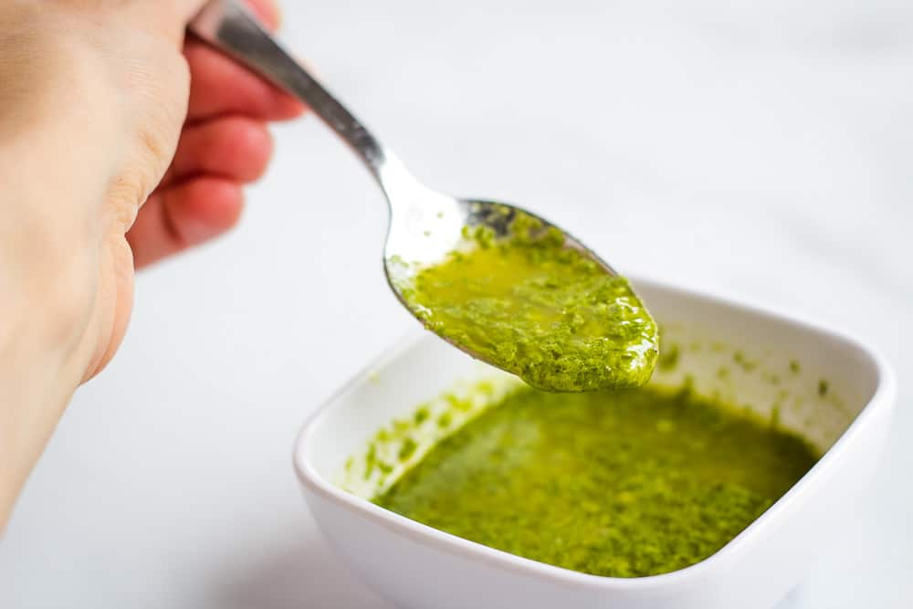Spoonful of basil sauce over small bowl.