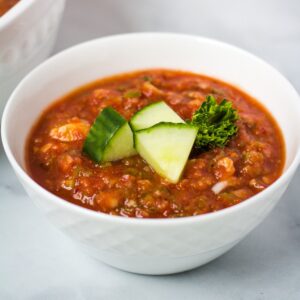 Bowl of vegan gazpacho topped with cucumber slices.