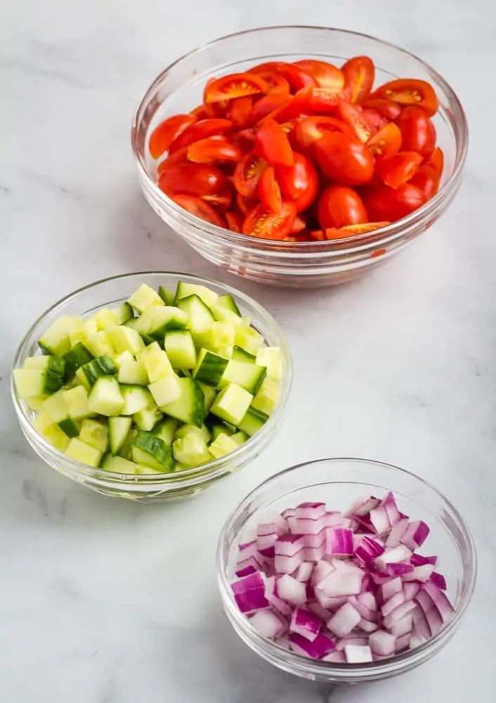 chopped tomatoes, cucumber, and red onion in glass bowls