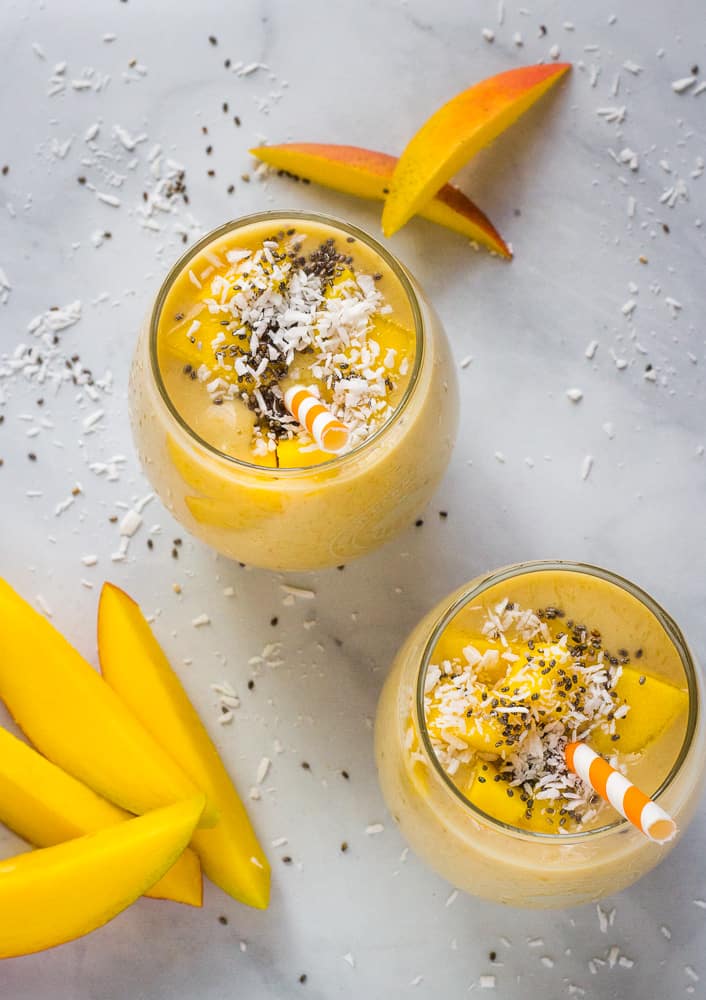 overhead of two mango smoothies with slices of mango