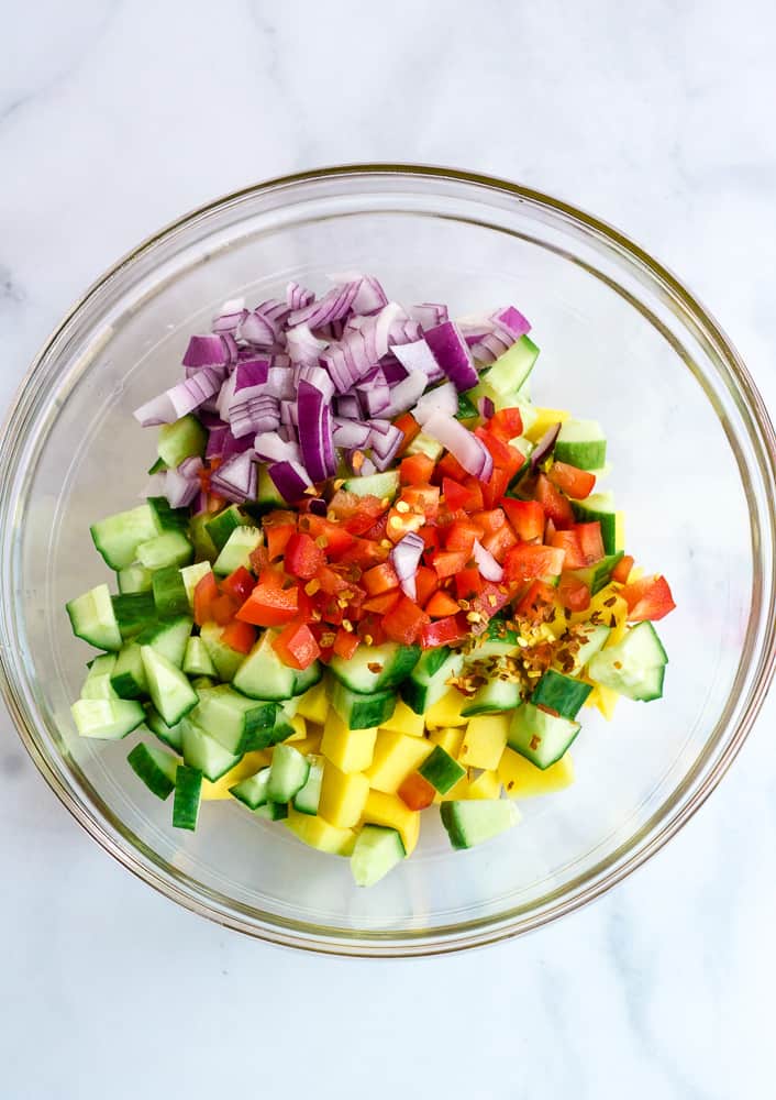 diced mangoes, cucumber, red onion, red pepper in glass bowl