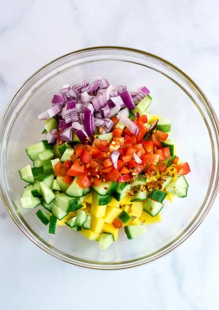 diced red onion, red pepper, cucumber, and mango in glass bowel