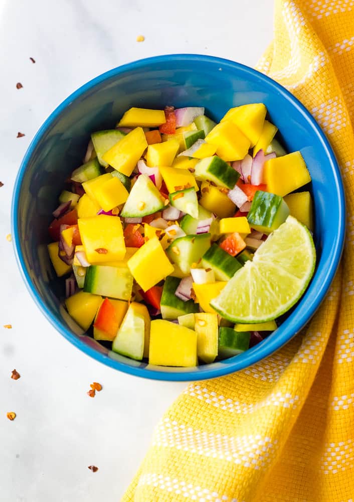 overhead of mango cucumber salad in blue bowl with yellow dish towel