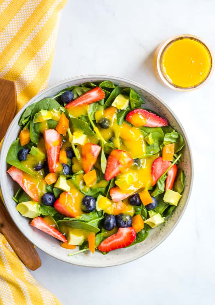 Overhead of berry salad with a side of mango dressing in a small jar. 