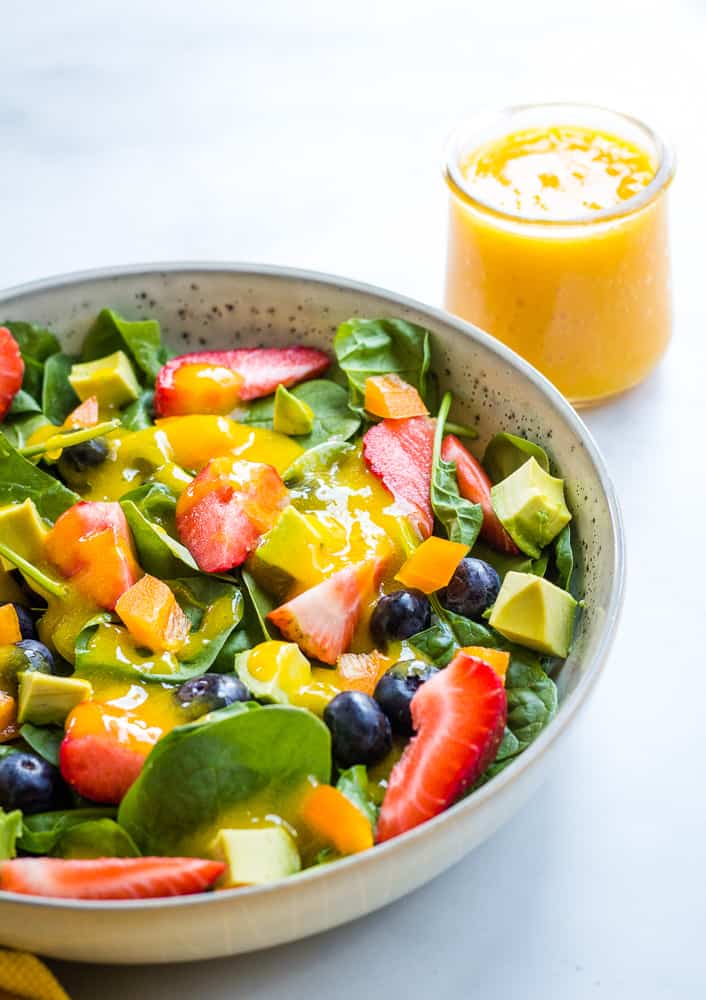 berry salad in gray bowl with mango dressing in background