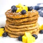 Stack of mango pancakes topped with cubed mango and blueberries.