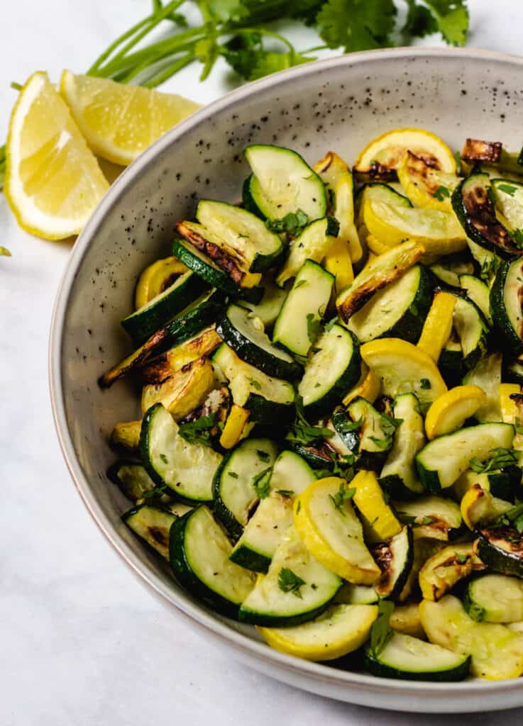 zucchini and yellow squash with fresh herbs and lemon in the background